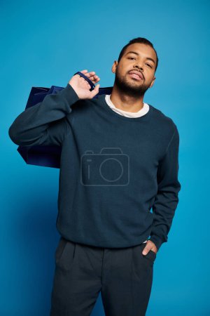 Foto de Joven afroamericano inclinado cabeza hacia atrás con bolsa de compras sobre hombro y mano en bolsillo - Imagen libre de derechos