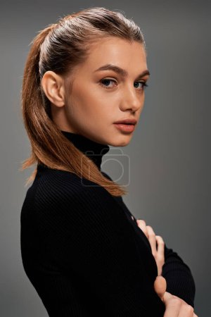 A young woman with long hair gracefully poses in a chic black turtleneck, exuding an aura of mystery and elegance.