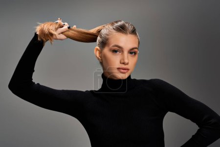 A young woman with blonde hair elegantly holds her hair in a ponytail.