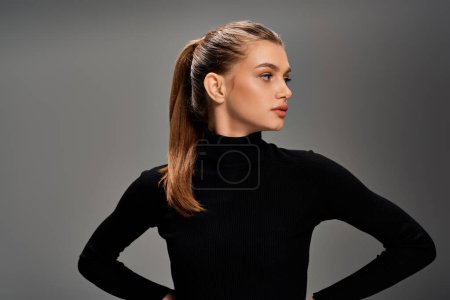 Eine junge schöne Frau mit langen welligen Haaren, die mit den Händen auf den Hüften in einer selbstbewussten und ausgeglichenen Haltung steht.
