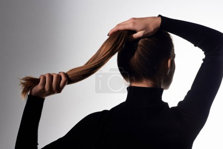 Appealing young elegant woman with long hair tied in a ponytail looks elegant and graceful.