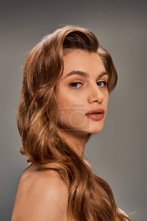 Foto de Una mujer joven con el pelo largo y ondulado marrón y ojos cautivadores mira a la distancia. - Imagen libre de derechos