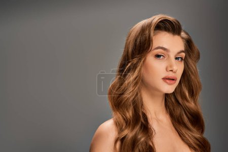 Photo for A young beautiful woman with long, wavy hair elegantly posing on gray backdrop - Royalty Free Image