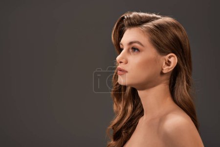 Eine junge Frau mit langen welligen Haaren posiert hemdlos und verkörpert natürliche Schönheit und Selbstbewusstsein.