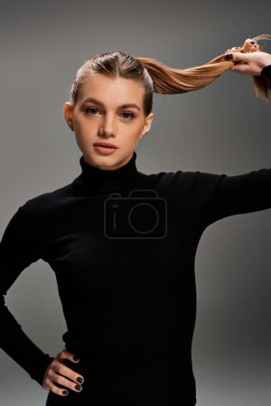 A young, beautiful woman in a black top gracefully holds her long hair, showcasing elegance and style.