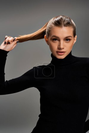 Photo for A young woman with long hair delicately touching her hair in her hand. - Royalty Free Image
