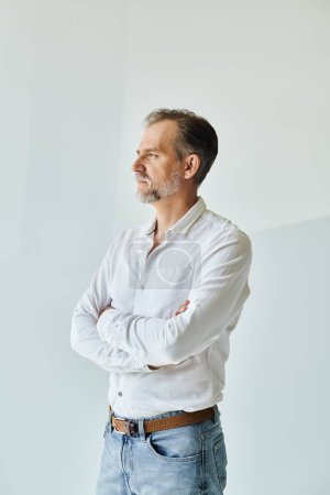 Portrait of mature handsome man in white shirt standing with his arms crossed and looking away