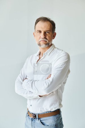 Portrait of mature handsome man in white shirt standing with his arms crossed and looking at camera