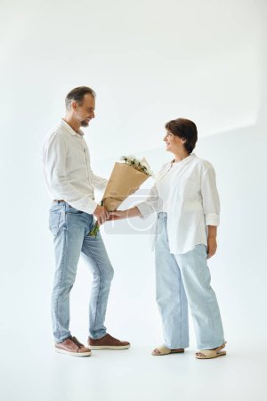 Photo for Full length shot of middle aged couple with flowers on grey background and looking at each other - Royalty Free Image