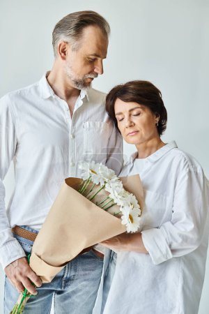 Téléchargez les photos : Portrait d'homme mature en chemise blanche présentant des fleurs à une jolie femme sur fond gris - en image libre de droit