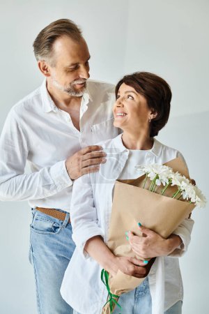 Téléchargez les photos : Portrait de couple mature souriant debout avec des fleurs sur fond gris - en image libre de droit