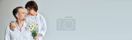 Photo for Portrait of happy mature couple with flowers on grey background, woman hugging man, banner - Royalty Free Image