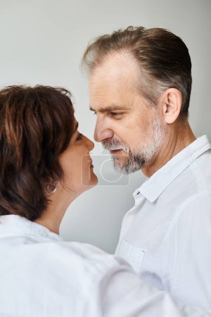 Foto de Retrato vista lateral de pareja madura enamorada abrazándose y besándose sobre fondo gris, cercanía - Imagen libre de derechos
