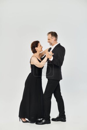Baile de salón pareja de mediana edad en una pose de baile y sonriente aislado sobre fondo gris