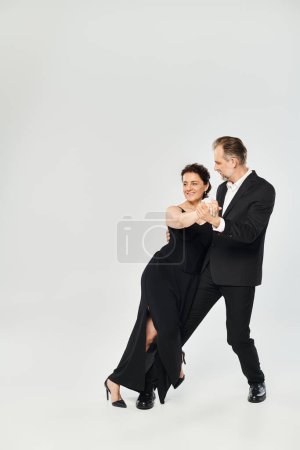 Foto completa de pareja atractiva madura en una pose de baile de tango aislada sobre fondo gris