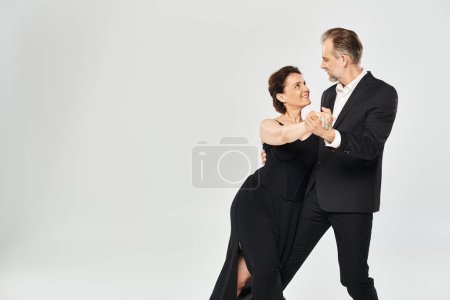 Téléchargez les photos : Danse de salon couple d'âge moyen dans une pose de danse et souriant isolé sur fond gris - en image libre de droit