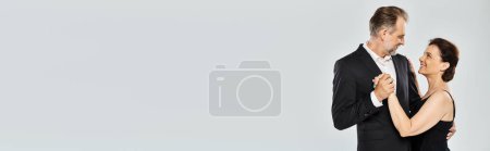 Téléchargez les photos : Danse de salon couple d'âge moyen dans une pose de danse et souriant isolé sur fond gris, bannière - en image libre de droit