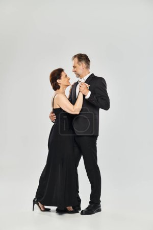 Baile de salón pareja de mediana edad en una pose de baile y sonriente aislado sobre fondo gris