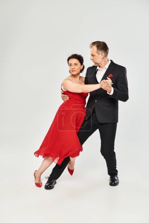 Ballroom dance middle aged couple in red dress and suit dancing tango isolated on grey background