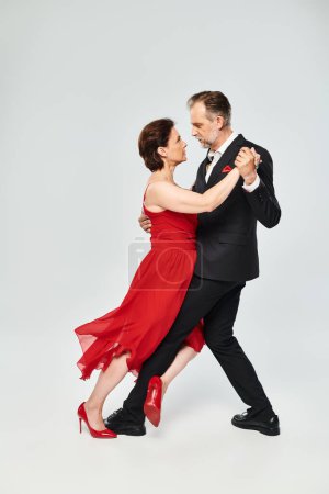 Danse de salon couple d'âge moyen en robe rouge et costume danse tango isolé sur fond gris