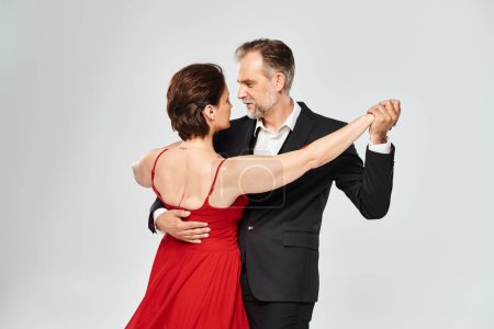 Mature attractive smiling couple dancing ballroom dance isolated on grey background