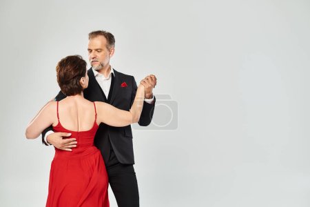 Edad media atractiva pareja apasionada bailando baile de salón aislado sobre fondo gris