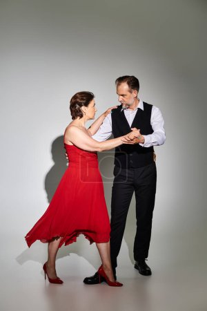 Ballroom dance middle aged couple in red dress and suit dancing tango isolated on grey background