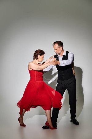 Téléchargez les photos : Danse de salon couple d'âge moyen en robe rouge et costume danse tango isolé sur fond gris - en image libre de droit