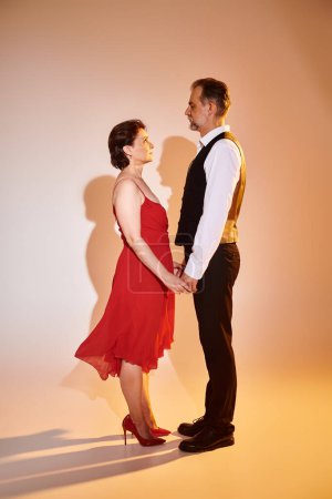 Mediana edad atractiva pareja sonriente bailarinas en vestido rojo y traje con luz amarilla sobre gris