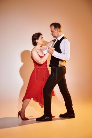 Ballroom dance middle aged couple in red dress and suit dancing tango with yellow light on grey