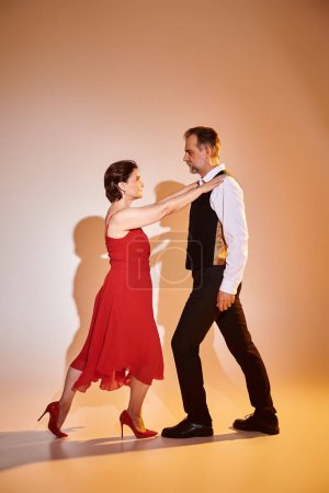 Retrato de pareja atractiva madura en vestido rojo y traje bailando sobre fondo gris