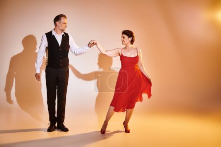 Baile de salón pareja de mediana edad en vestido rojo y traje bailando tango con luz amarilla sobre gris