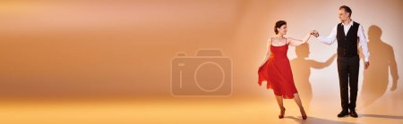 Ballroom dance mature couple in red dress and suit dancing tango with yellow light on grey, banner