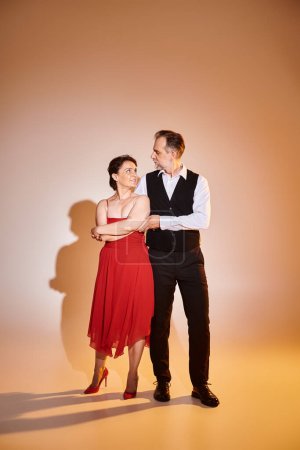Portrait of middle aged attractive couple in red dress and suit standing on grey background
