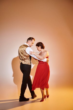 Portrait de couple séduisant mature en robe rouge et costume dansant sur fond gris