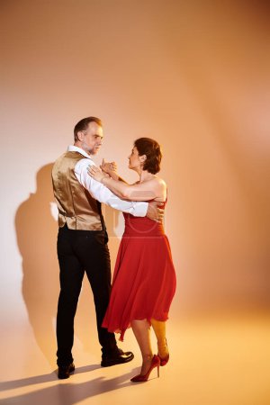 Standardtanz Paar mittleren Alters in rotem Kleid und Anzug tanzt Tango mit gelbem Licht auf grau