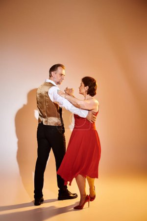 Retrato de pareja atractiva madura en vestido rojo y traje bailando sobre fondo gris