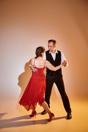 Full length image of mature attractive couple in red dress and suit dancing on grey background
