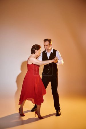 Standardtanz Paar mittleren Alters in rotem Kleid und Anzug tanzt Tango isoliert auf grauem Hintergrund