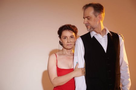 Mature couple standing and hugging in elegant outfits with yellow light on grey background