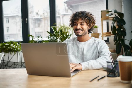 Photo for A man of diverse background sits intently in front of a laptop computer in a modern coworking space, engaging in digital work. - Royalty Free Image