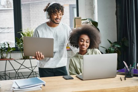 Ein multikultureller Mann und eine multikulturelle Frau, die sich auf Laptops konzentrieren und in einem modernen Büro-Coworking-Space zusammenarbeiten.