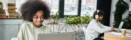 Foto de Una mujer de ascendencia diversa se sienta en un profundo pensamiento frente a una computadora portátil, inmersa en el trabajo o el estudio, en un moderno espacio de coworking. - Imagen libre de derechos
