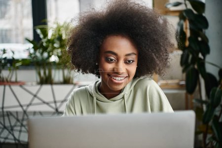 Eine schwarze Frau, die in der Arbeit versunken vor einem Laptop in einem modernen Coworking Space sitzt.