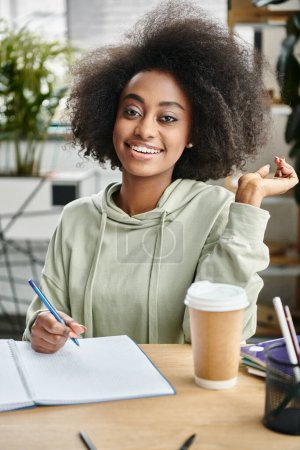 Une femme dans un moment serein, assise à une table avec un cahier et un stylo, absorbée par la pensée et capturant des idées.