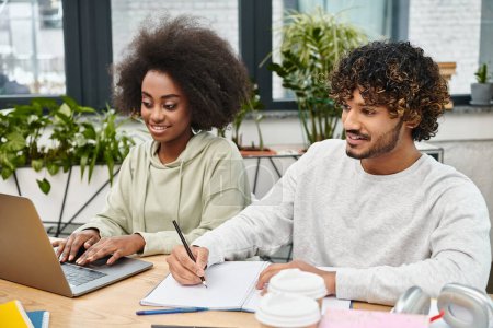 Deux personnes, représentant la diversité culturelle, s'assoient à une table avec un ordinateur portable, engagées dans une étude collaborative.
