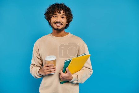 Un homme, vêtu avec désinvolture, tenant un livre et une tasse de café.