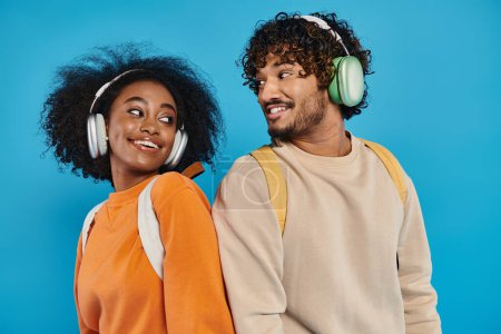 Ein gemischtrassiges Paar steht zusammen, trägt Kopfhörer und teilt Musik auf blauem Hintergrund in einem Studio-Setting.
