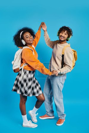 A young interracial couple, standing close together in casual attire, exuding harmony and togetherness on a blue backdrop.