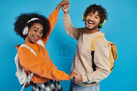An interracial man and woman dance together, wearing headphones, expressing joy and connection through movement on a blue backdrop.